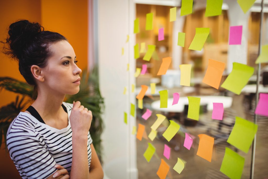 Beautiful female executive reading sticky notes in office